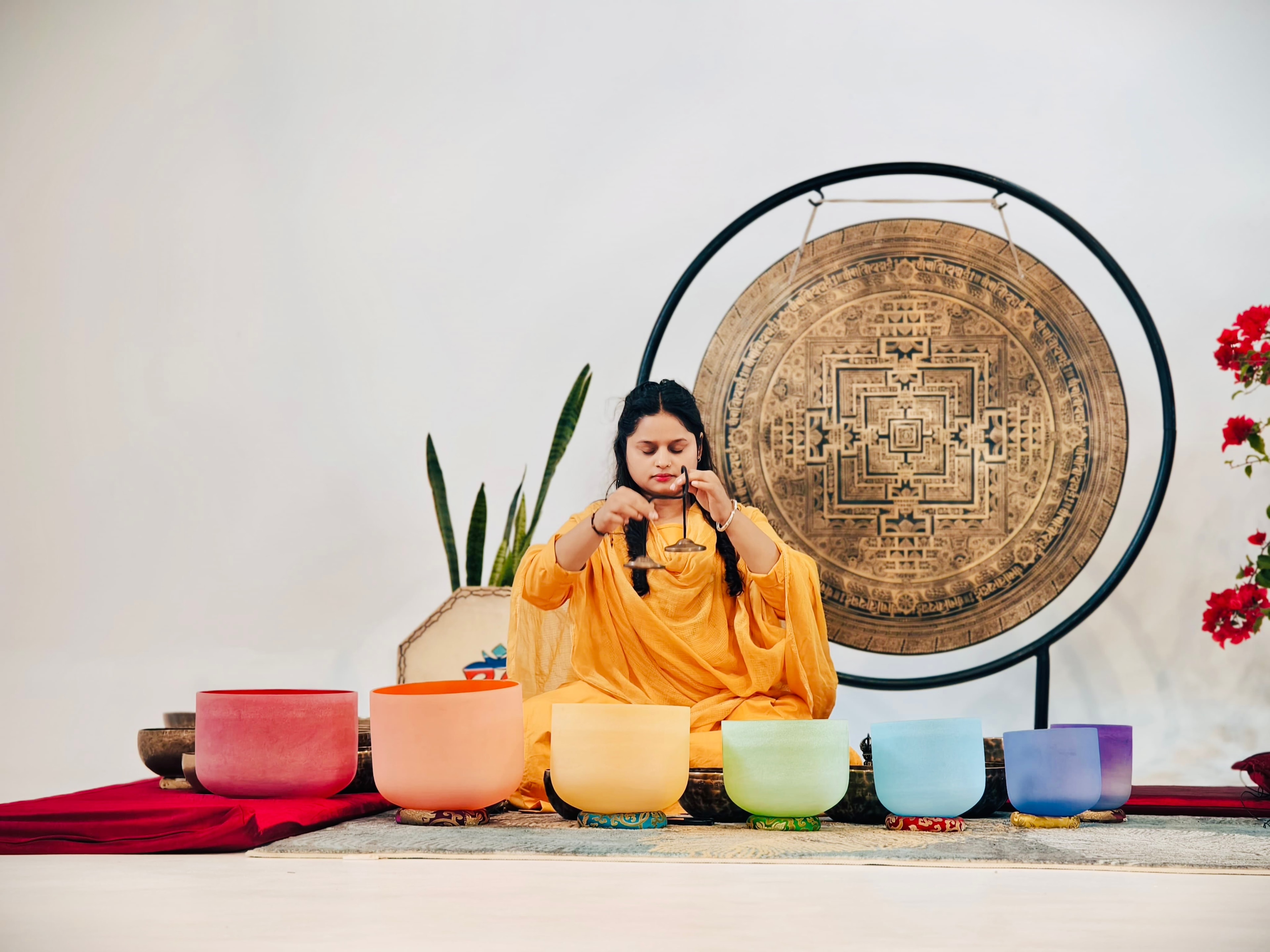 A practitioner playing crystal singing bowls in front of a large gong