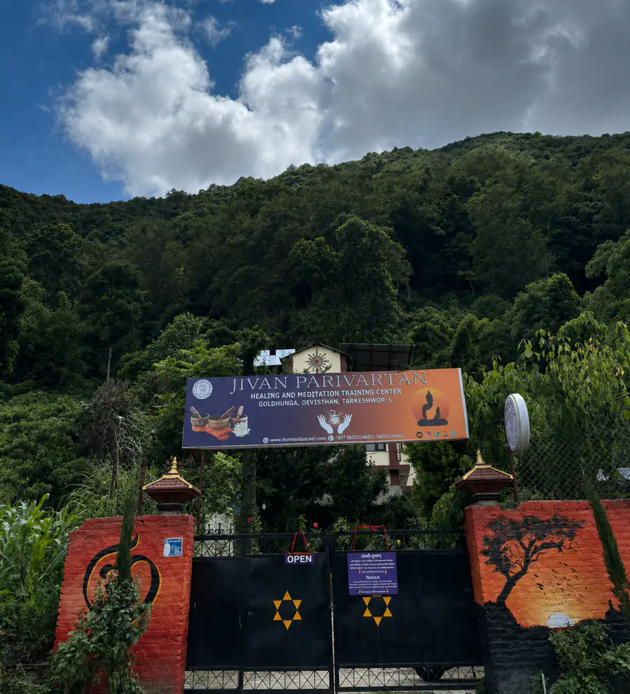 The entrance gate and signboard of Jivan Parivartan at Goldhunga, Devisthan, Tarkeshwor-5, with the forested Nagarjun hillside behind it