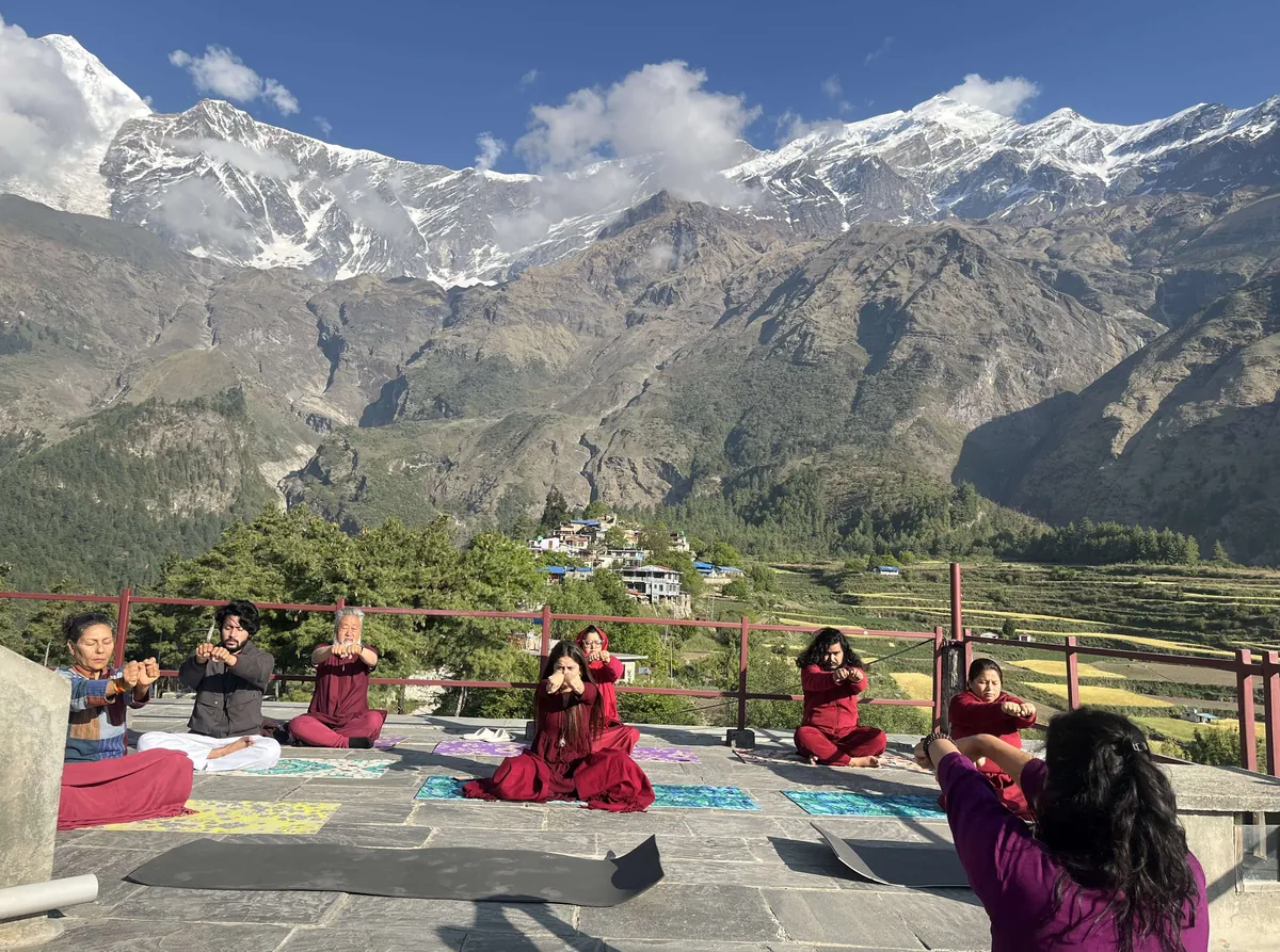 Guests practising yoga on a terrace above the valley with the Himalaya behind them