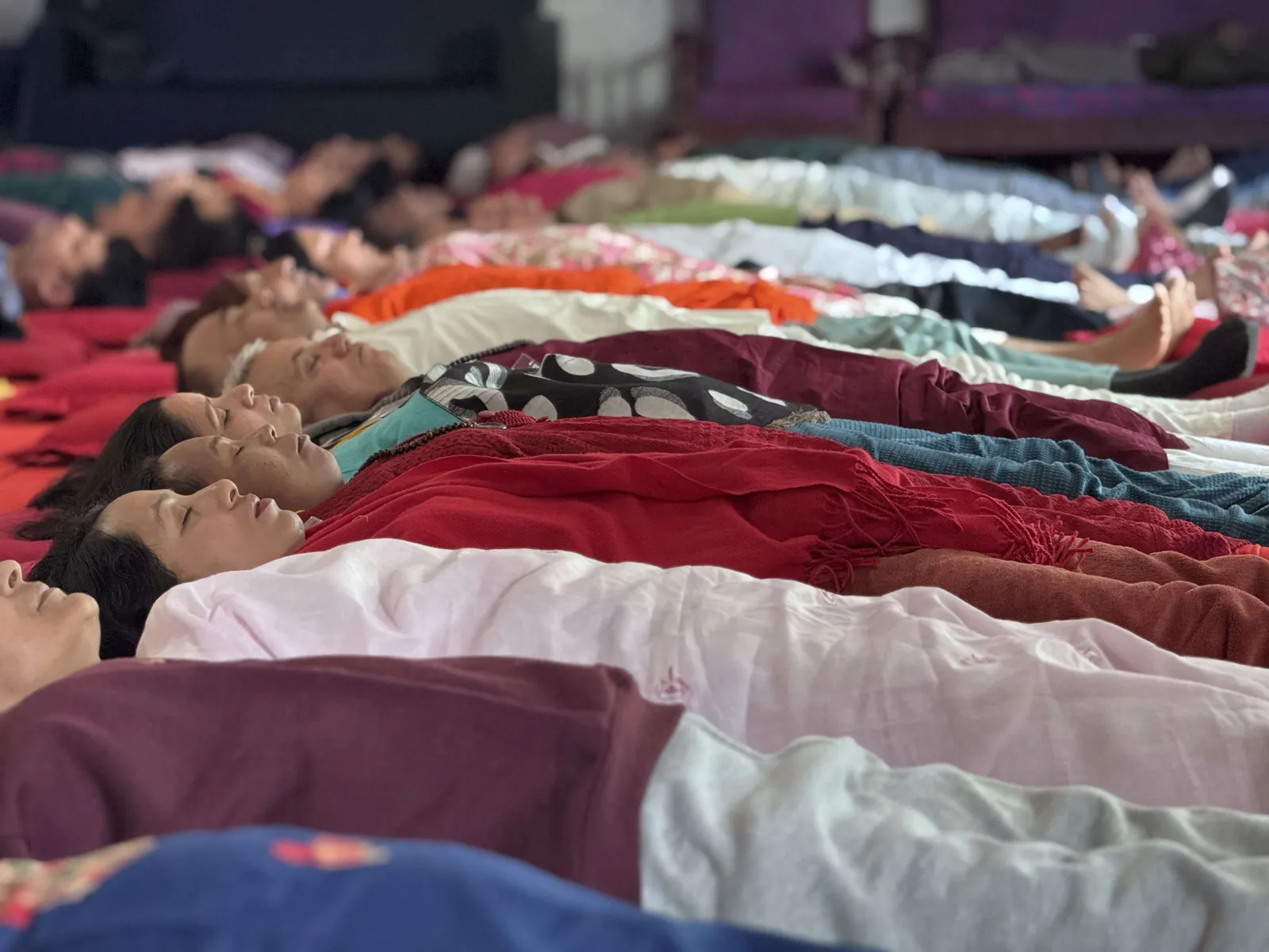 A close row of participants lying with eyes closed and heads on cushions during a guided relaxation