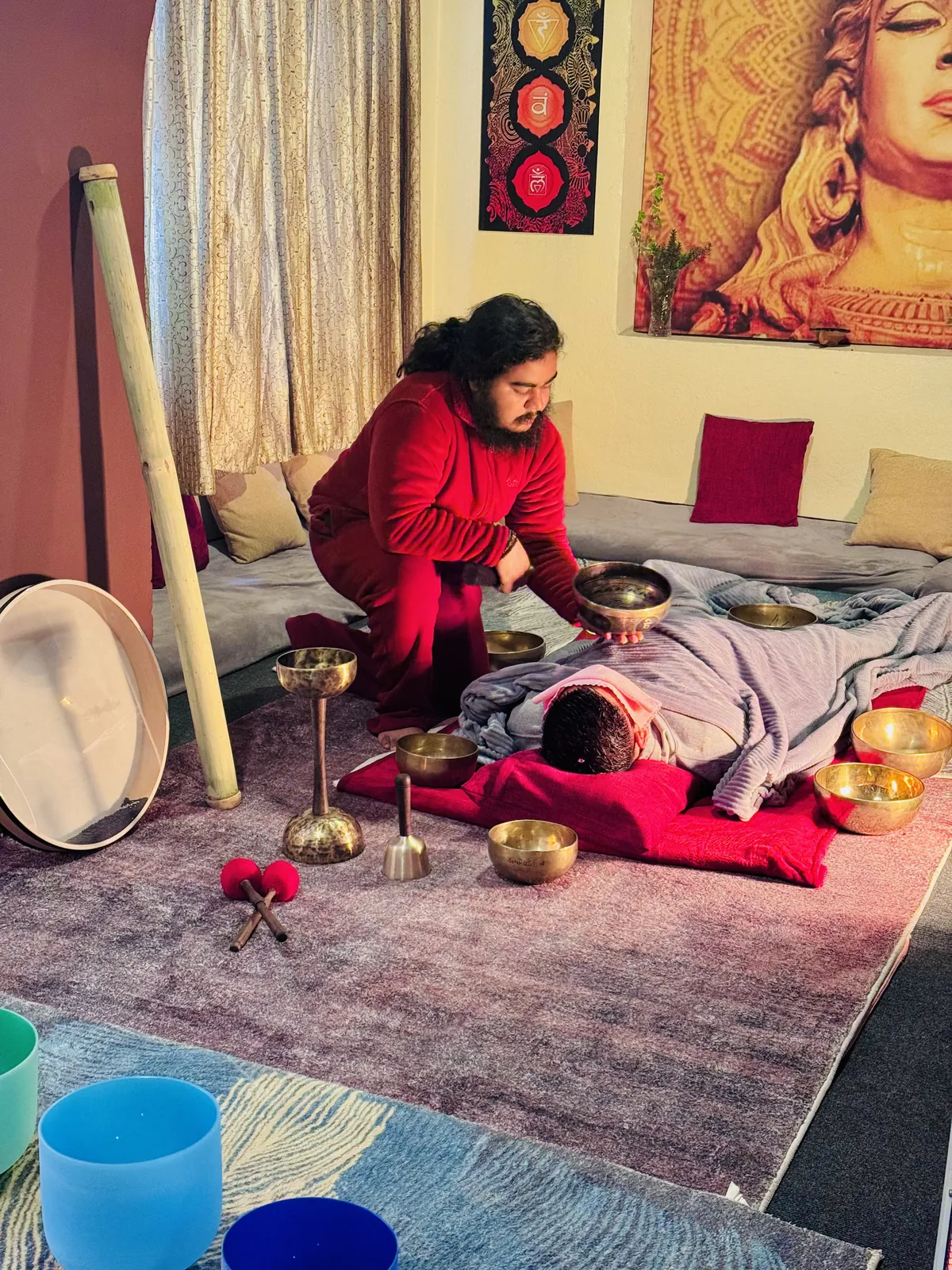 A practitioner holding a hammered metal singing bowl over a resting guest