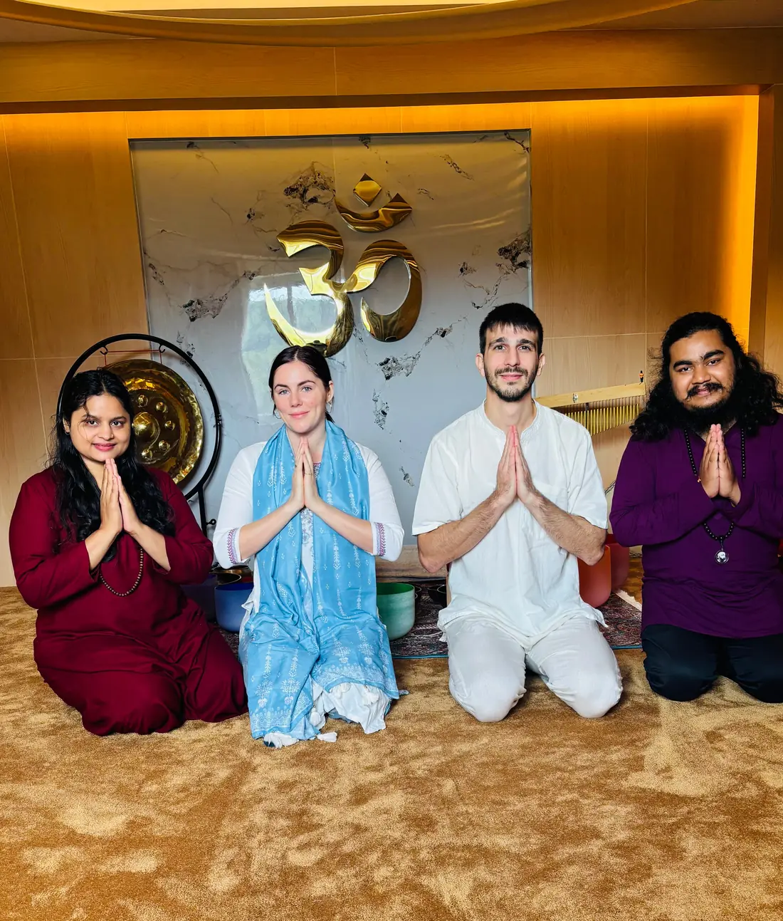 Four practitioners kneeling in namaste before the golden Om, gong and singing bowls in the meditation hall at Jivan Parivartan, Kathmandu