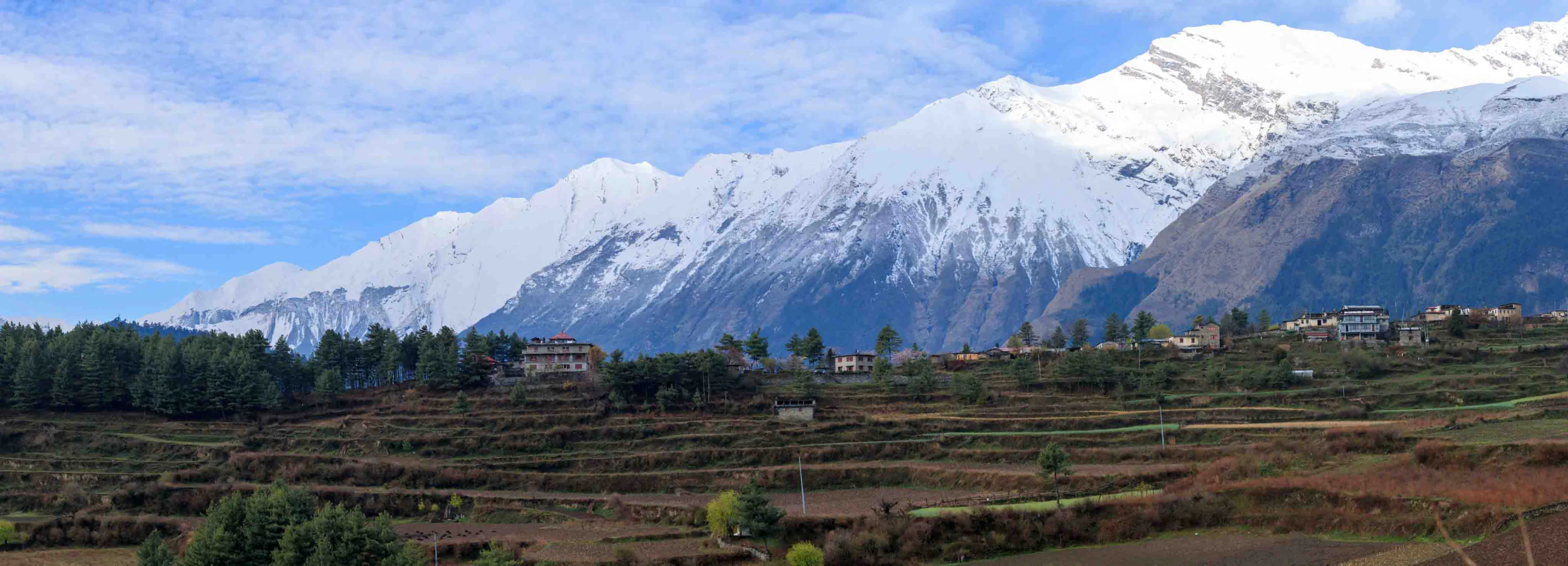 Snow-capped Himalayan peaks rising above a hillside village and terraced fields, Nepal