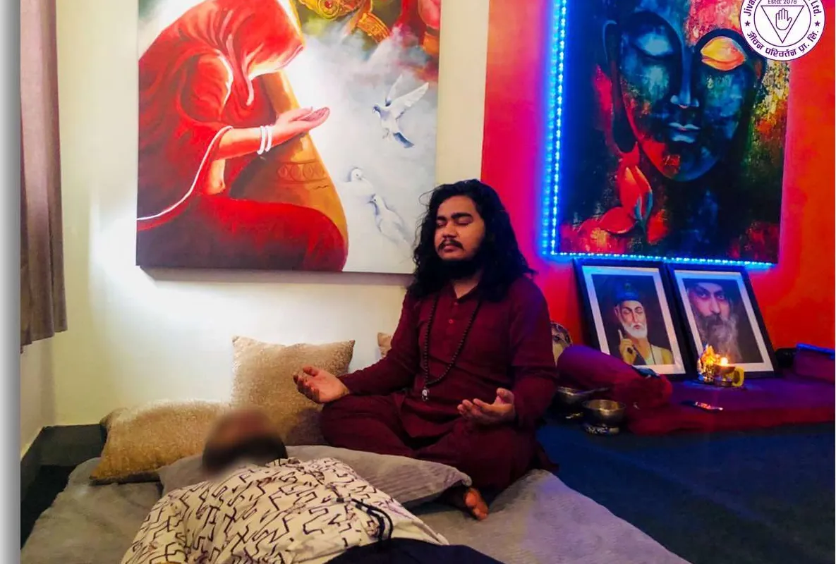 A Reiki practitioner seated in meditation beside a resting client during an attunement
