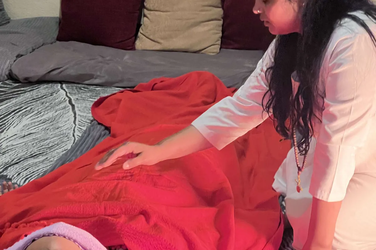 A practitioner giving hands-on Reiki to a client resting under a blanket