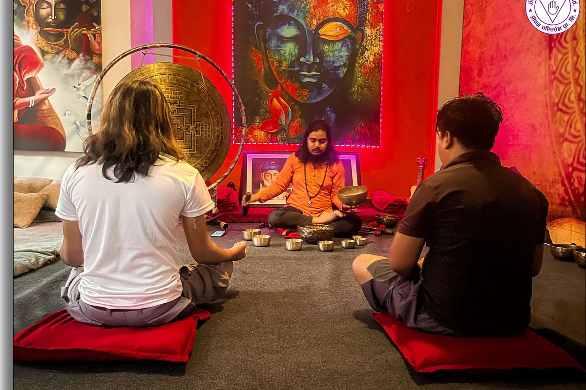 Two students learning to play Himalayan singing bowls with their teacher, gong behind them